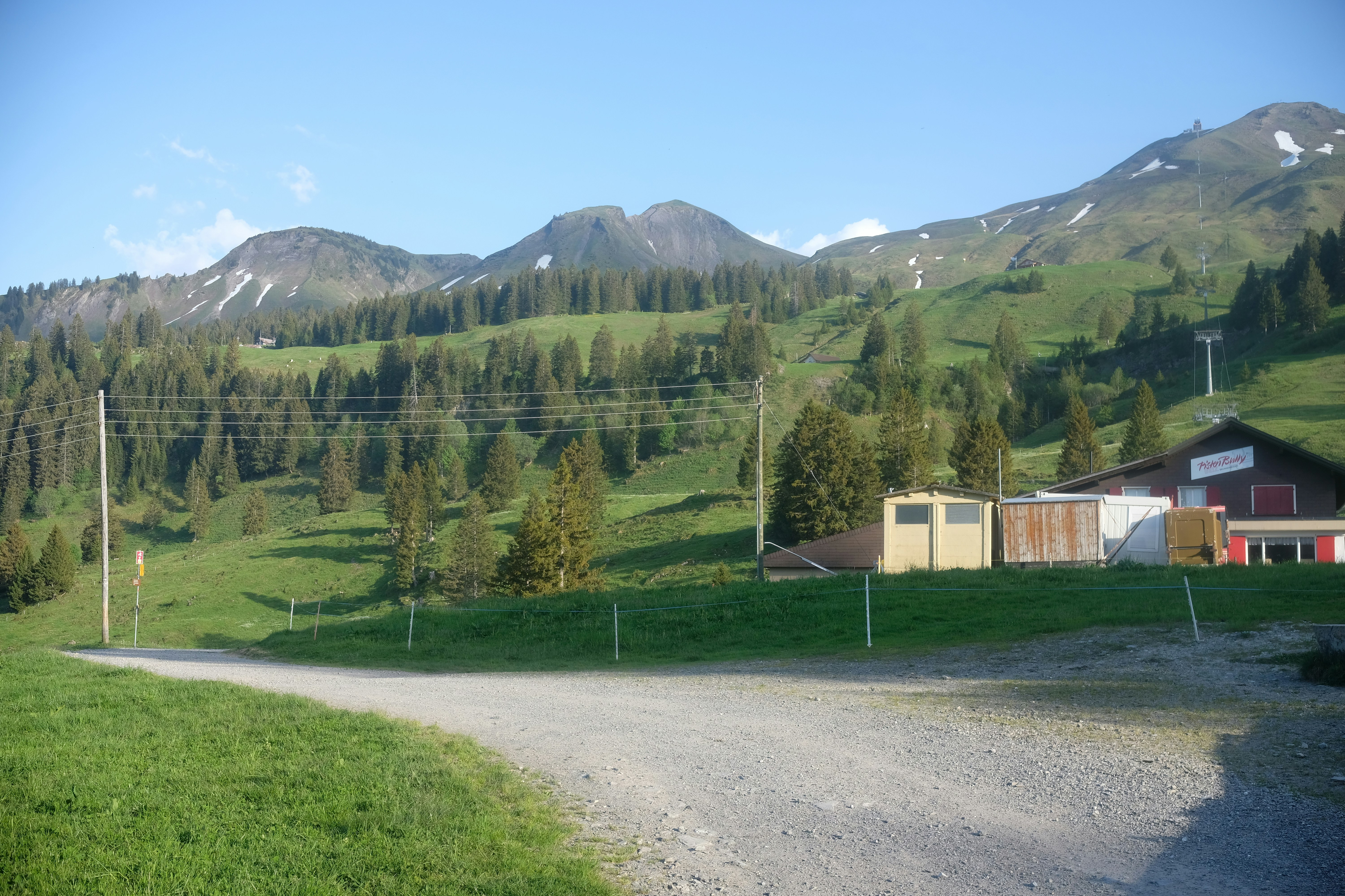 A dirt road leads through green hills towards snow-capped mountains.